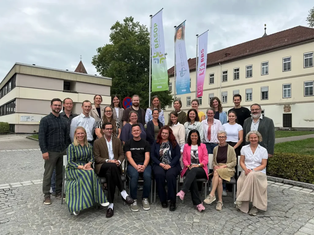 Gruppe von 26 Personen steht vor einem Gebäude mit Fahnen in Österreich.